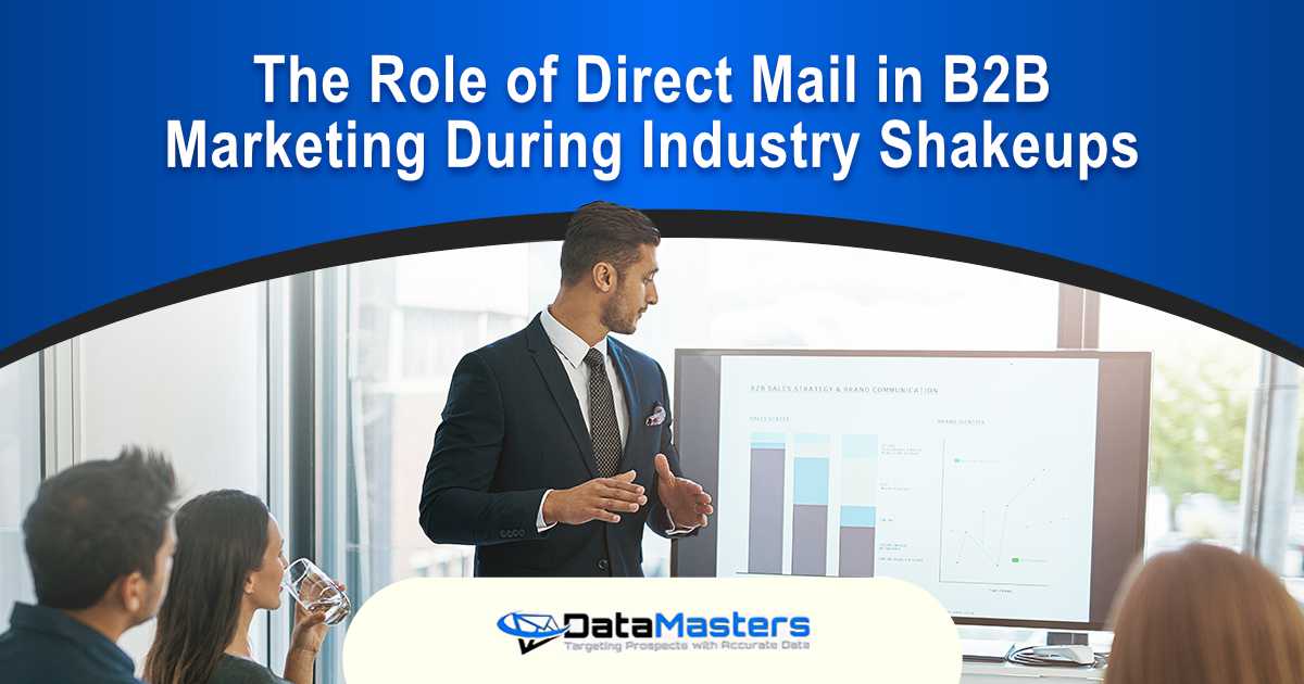 Image of a businessman giving a presentation with a monitor and whiteboard displaying graphs to a group in an office, featuring Datamasters and highlighting the role of direct mail in B2B marketing during industry shakeups.