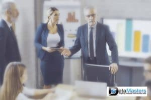 Group of business people, male and female standing and seated around a table with charts in the background.