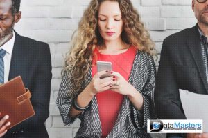 Young woman looking down at cell phone and two males on either side of her.